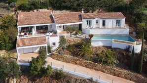 A two-story house with a swimming pool, surrounded by stone walls and greenery.