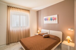 A bedroom with a bed, curtains, a wall art piece, and two bedside lamps. - Villa Apartment with private pool and unobstructed Sea Views (Marsaskala)