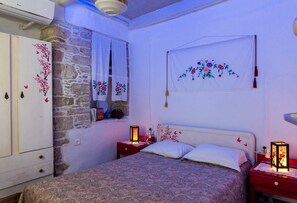 Una camera da letto con un letto, due comodini, una finestra con tende e un arazzo appeso al muro, oltre a una parete in pietra.