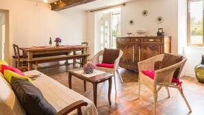 Uma sala de estar acolhedora com uma mesa de jantar de madeira, cadeiras de vime, um sofá e um armário.