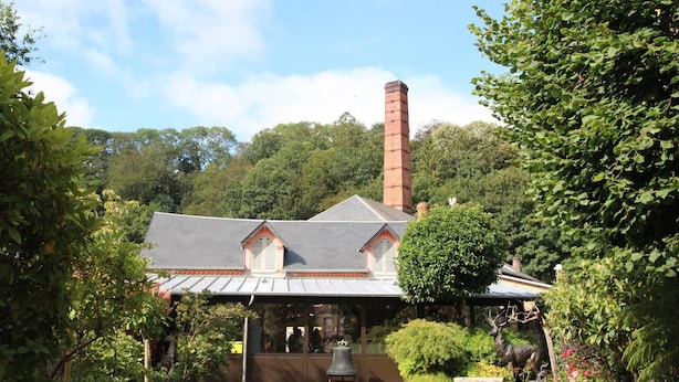 Um edifício com chaminé, varanda coberta e jardim com estátuas.