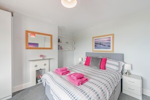 Quarto com cama, mesas de cabeceira, espelho, lareira e uma estante com livros.