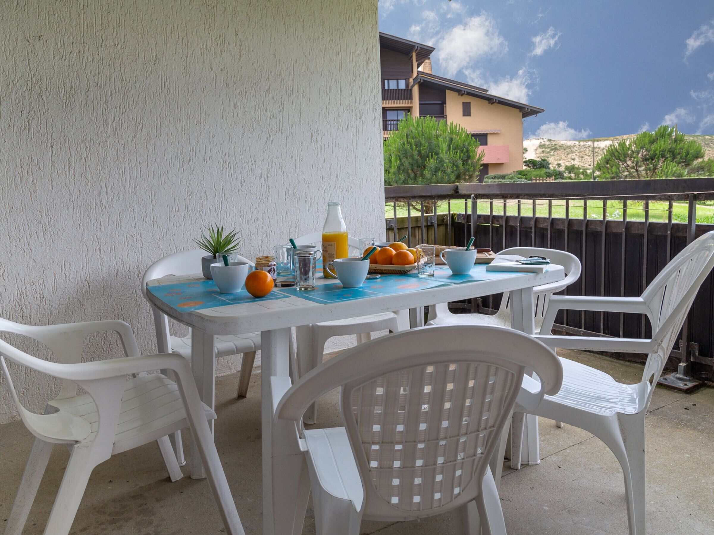 A patio with a table set for breakfast, white plastic chairs, and a view of a building in the background.