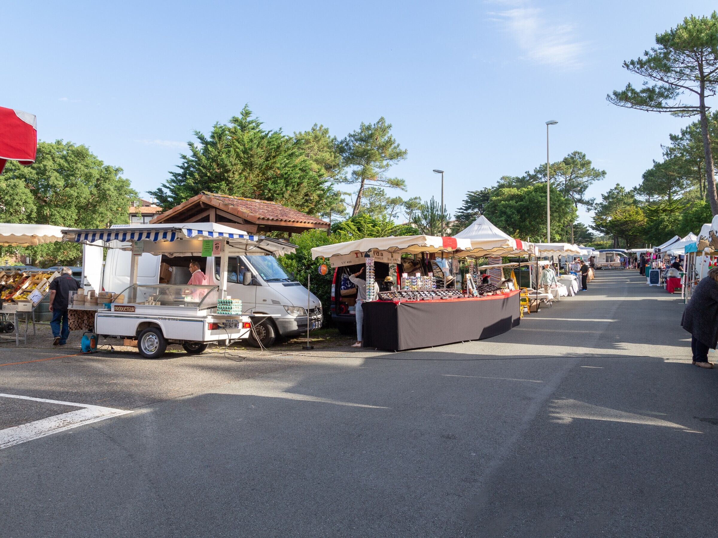 Un marché de rue avec différents étals et un fourgon blanc.
