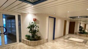A spacious lobby with a marble floor, a large potted plant, and a fire alarm on the wall.