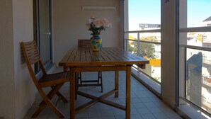 A balcony with a wooden table and chairs, a vase with flowers, and a view of buildings.