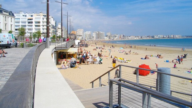 A beach with people sunbathing and walking along the promenade.