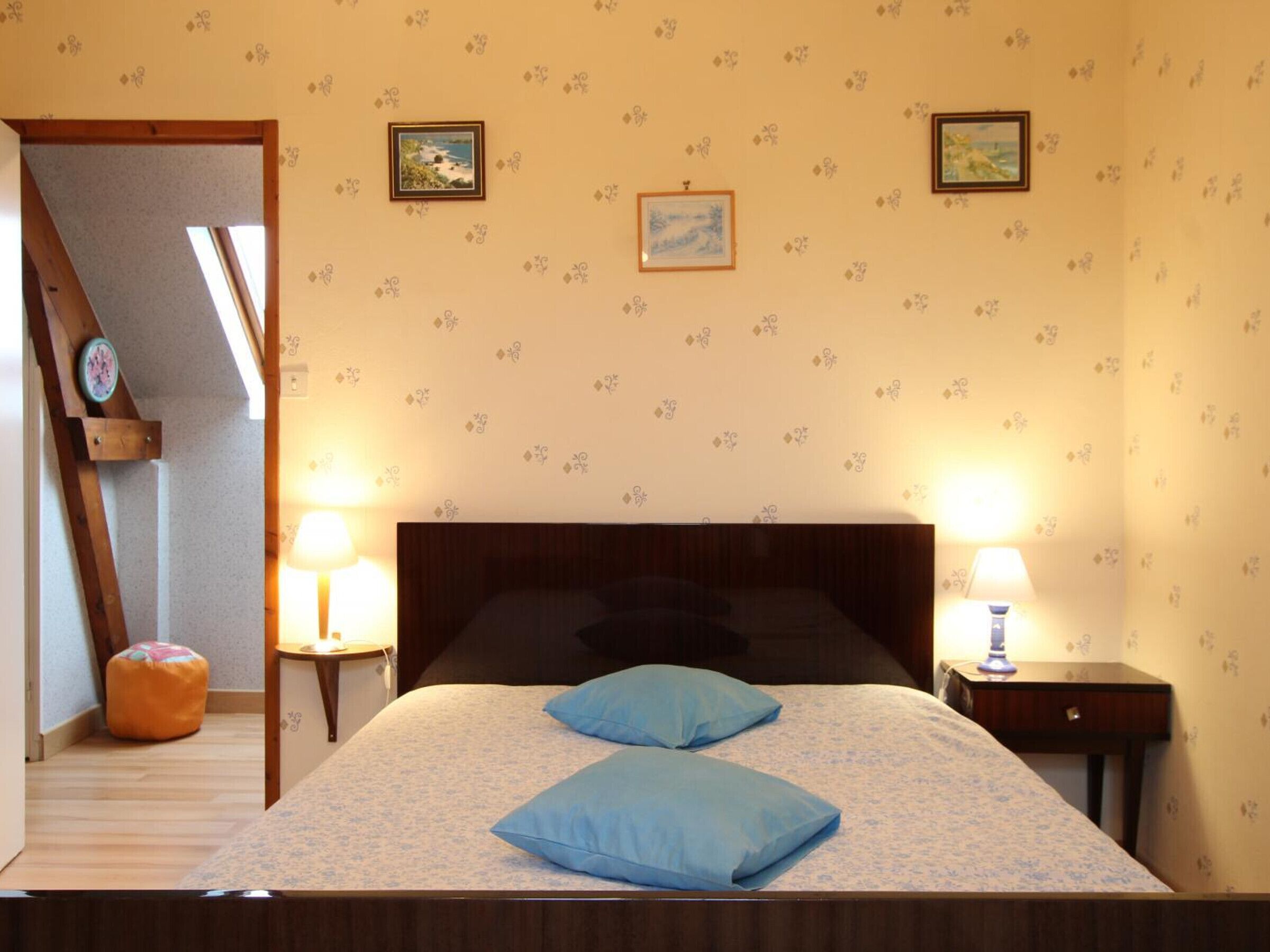 Un dormitorio con una cama, dos lámparas de noche, un cabecero de madera y un taburete pequeño de madera.