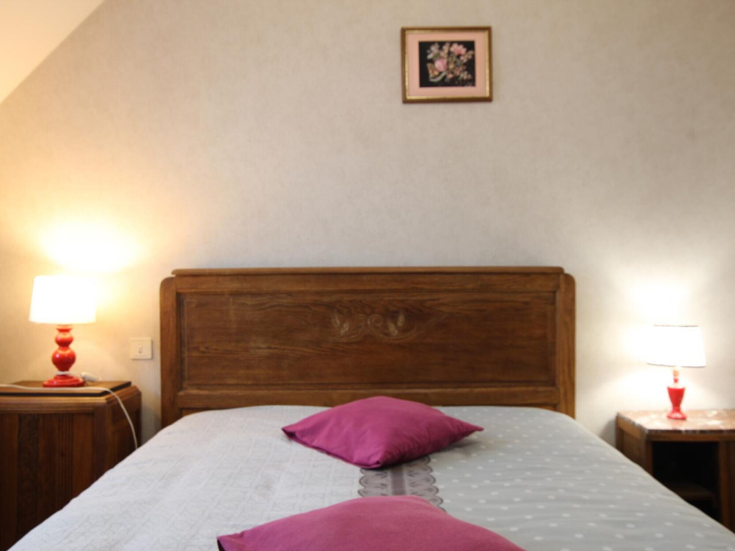 A neatly made bed with a wooden headboard, two pillows, and bedside lamps on wooden nightstands.