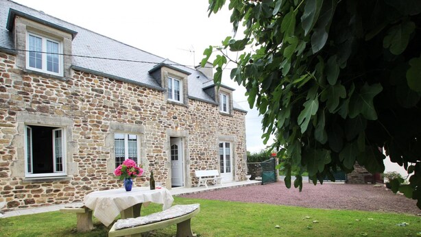 A stone building with a grassy yard, a bench, and a table with flowers.