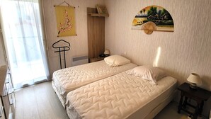 A bedroom with two beds, a radiator, a hanging chair, and a wall-mounted fan. - Charming apt with terrace, parking, near beach and shops (Les Sables-d'Olonne)
