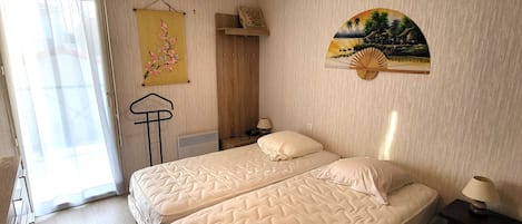 A bedroom with two beds, a radiator, a hanging chair, and a wall-mounted fan.