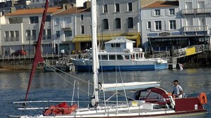 A sailboat docked at a marina with buildings in the background. - Charming apt with terrace, parking, near beach and shops (Les Sables-d'Olonne)