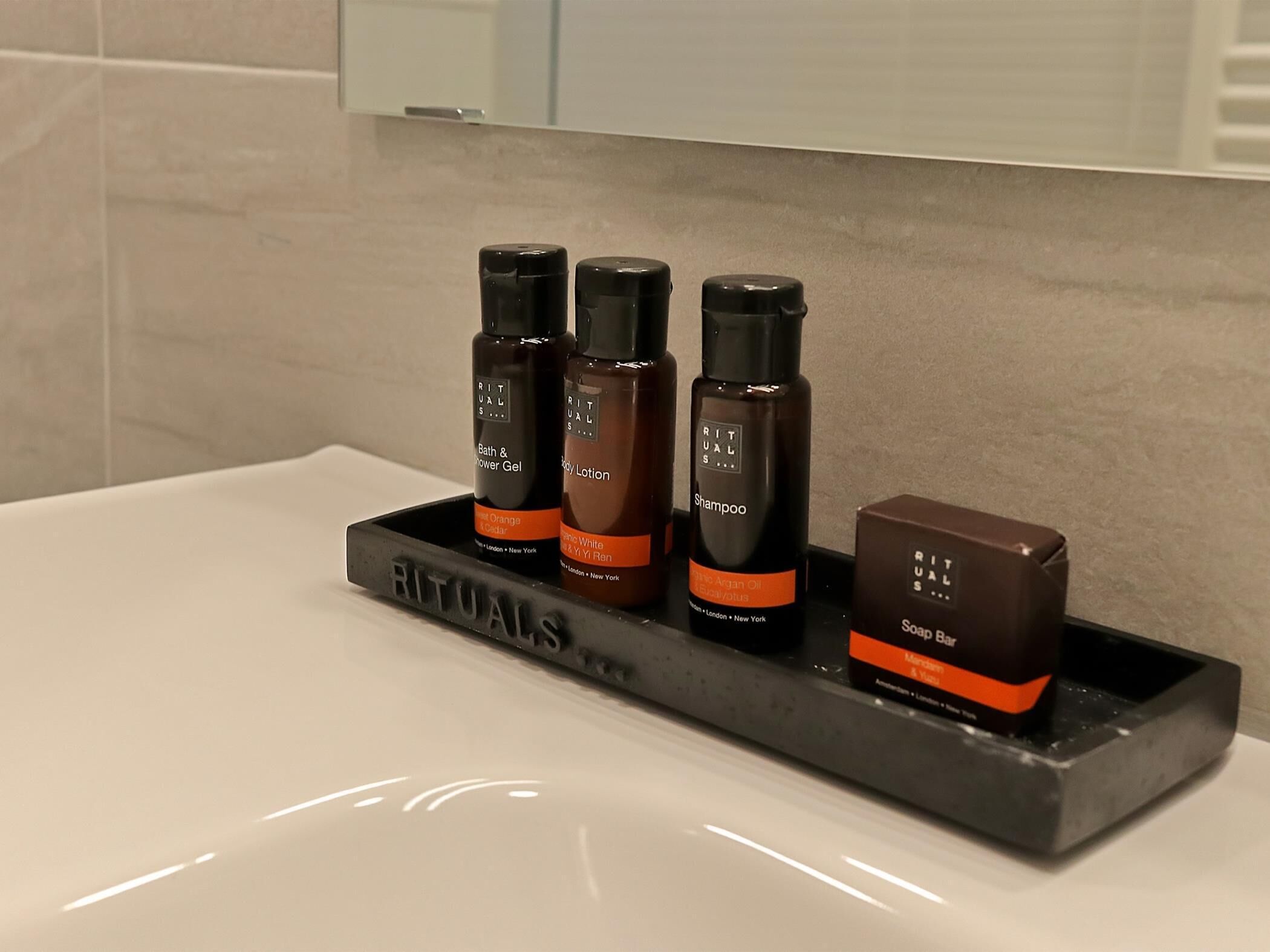Un baño con una bandeja negra que contiene cuatro productos de Rituals para el cuidado corporal.