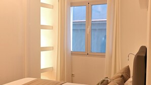 Een slaapkamer met een bed, een raam en een nachtkastje met een lamp.