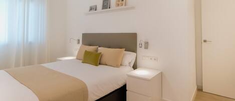 A modern bedroom with a bed, bedside tables, a nightstand, a door, and a shelf with pictures.
