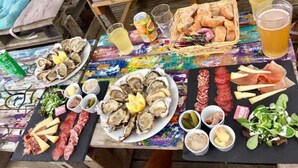Ein Tisch reich gedeckt mit Austern, verschiedenen Fleischsorten, Brot und Getränken, der eine Mahlzeit andeutet.