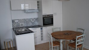 Una cocina compacta con armarios blancos, horno empotrado y una mesa de comedor con cuatro sillas.