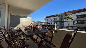 Ein Balkon im Freien mit einem Holztisch und -stühlen, Blick auf moderne Gebäude und einem strahlend blauen Himmel.