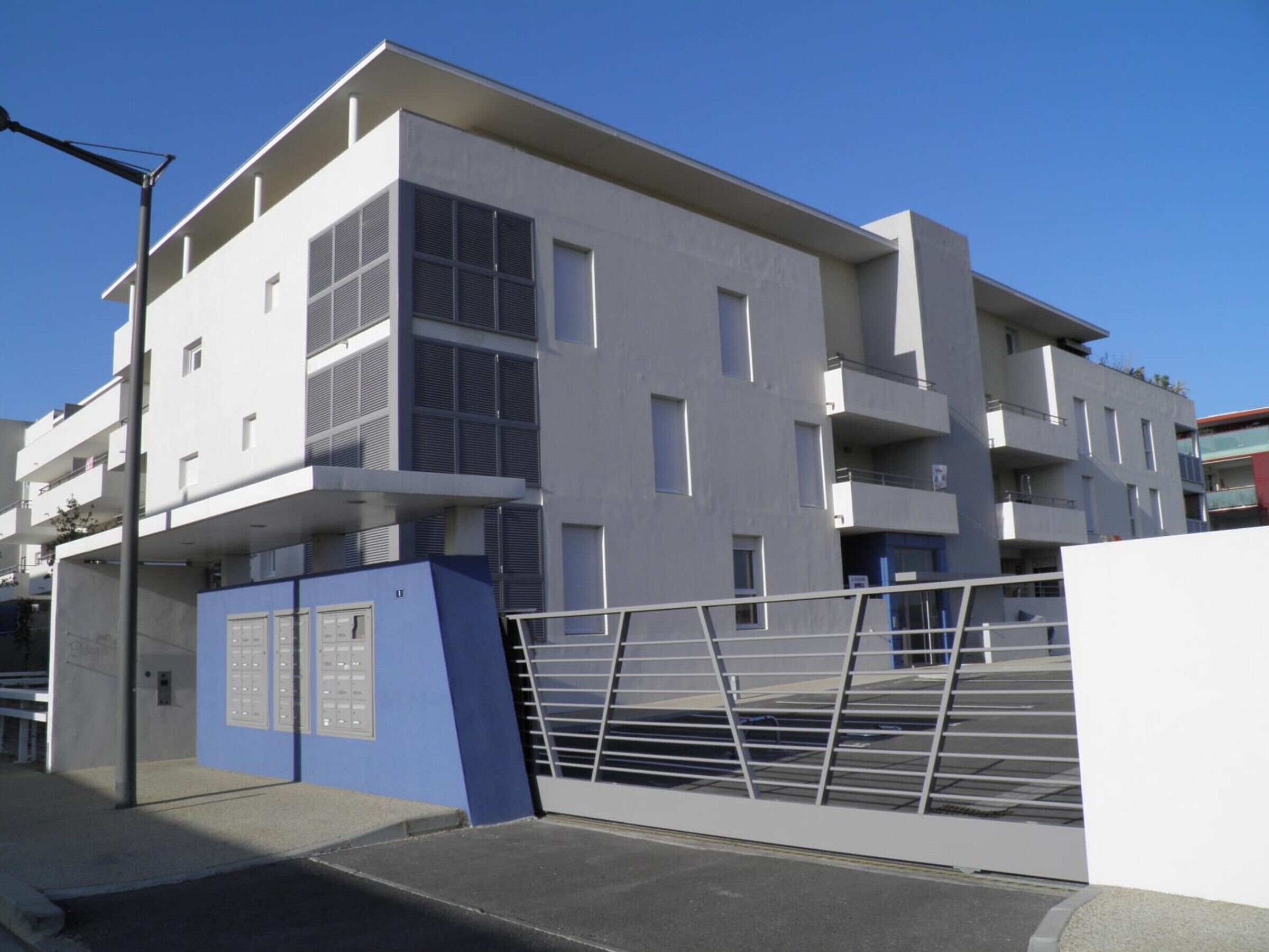 Un immeuble moderne à plusieurs étages, doté d’une façade sobre, de balcons et d’une entrée sécurisée par un portail.