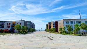 Ein weitläufiger Innenhof mit modernen Gebäuden, Palmen und blauem Himmel.