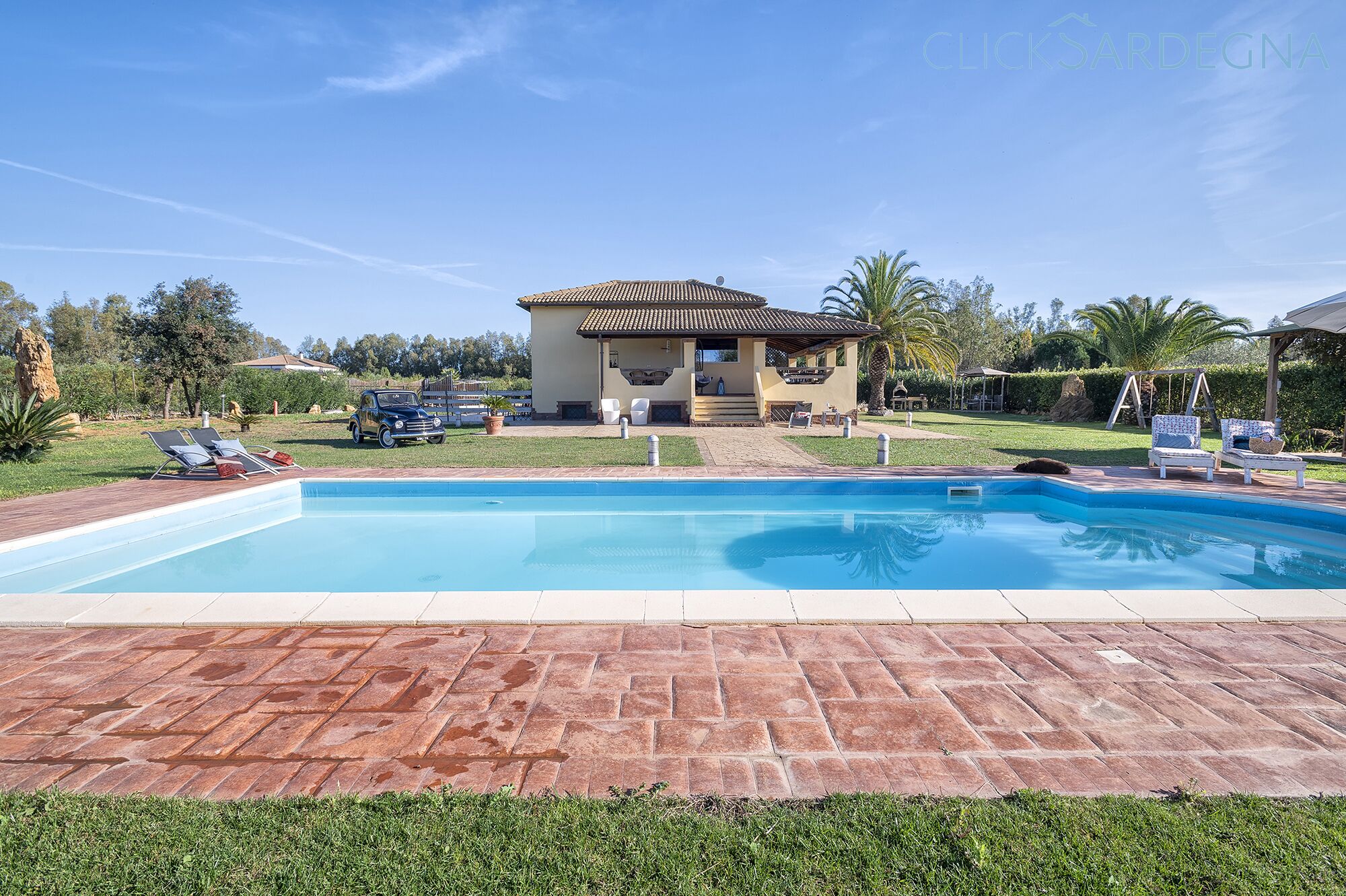 A swimming pool with lounge chairs and a classic car parked nearby.