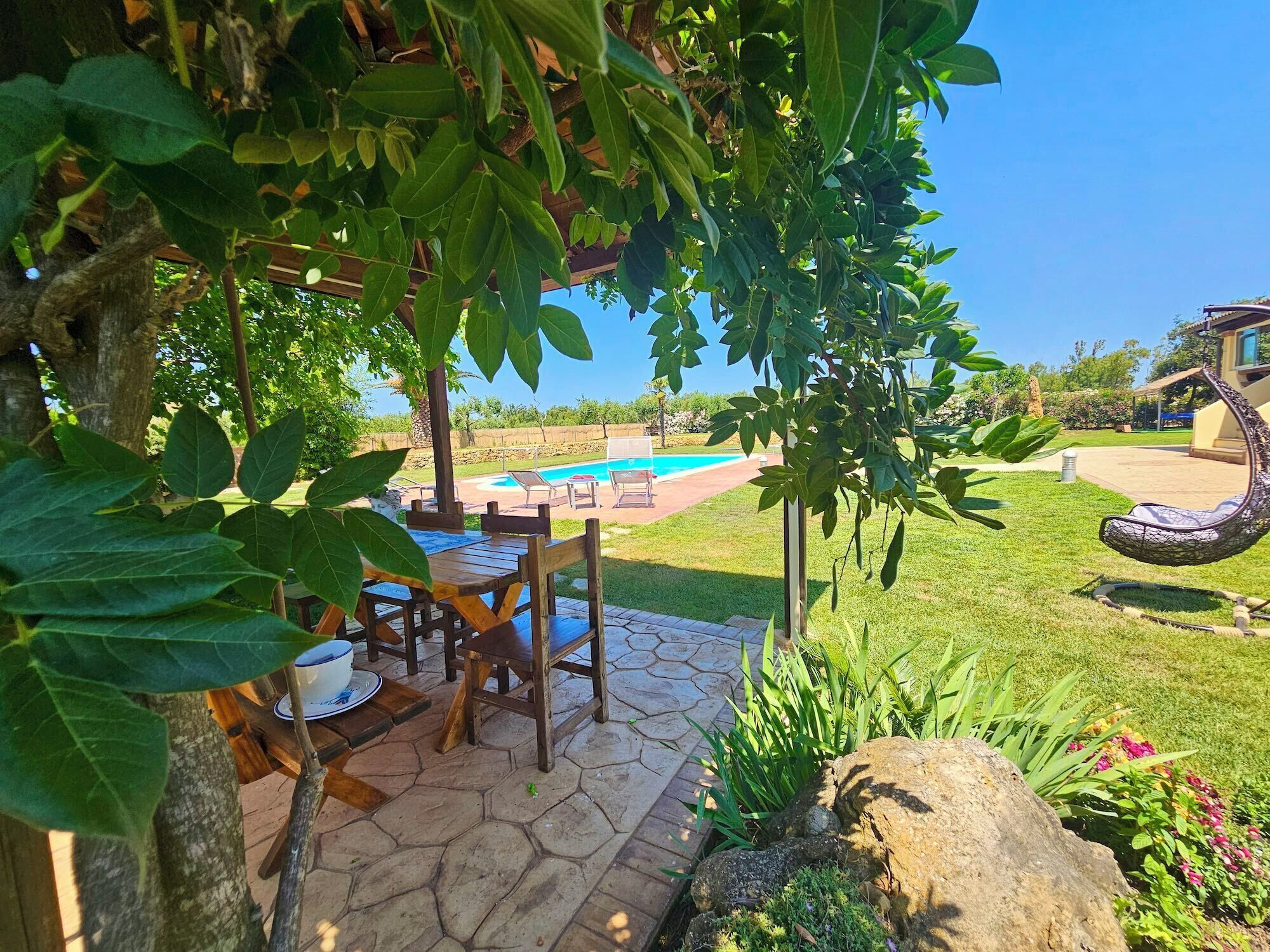 Une terrasse avec une table et des chaises, une piscine et un fauteuil suspendu.