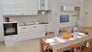 A modern kitchen with white cabinetry, a built-in oven, and a dining area with a wooden table set for four.