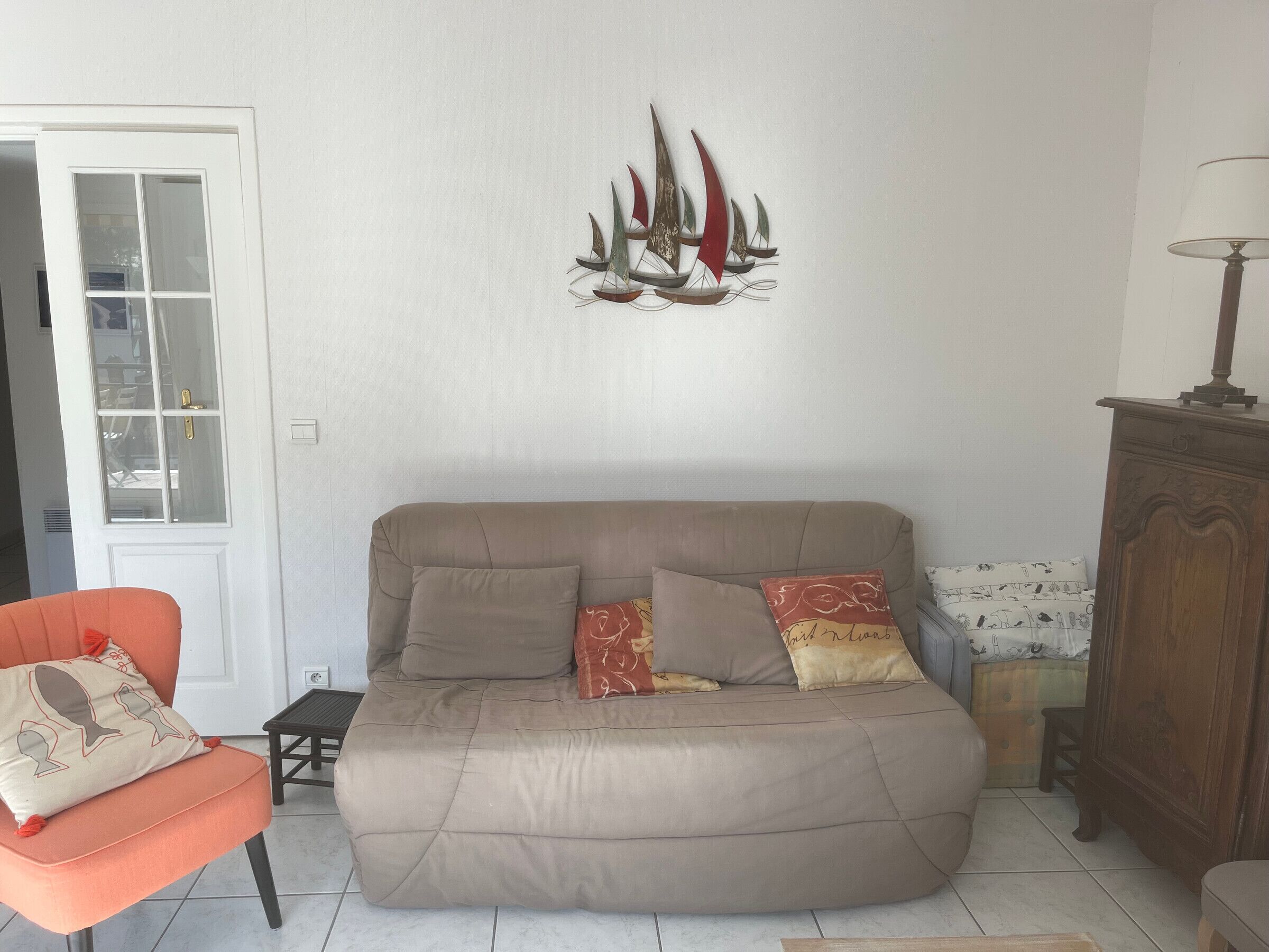 A living room with a beige sofa, orange armchair, and a decorative sailboat wall art piece.