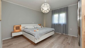 Une chambre moderne avec un grand lit, des tables de chevet, un luminaire décoratif au plafond et une fenêtre avec des rideaux.