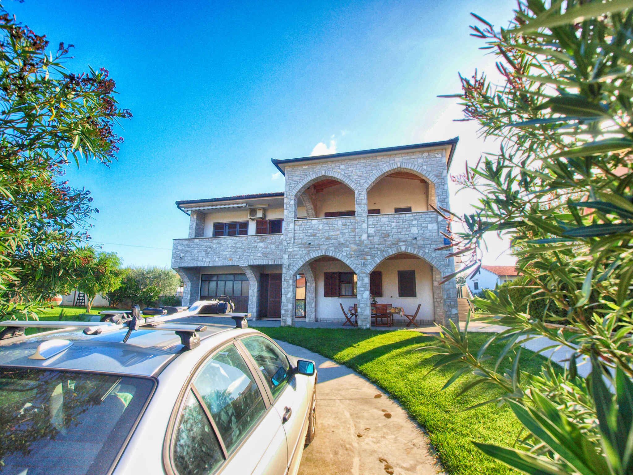 A two-story stone house with a driveway, parked cars, and a well-maintained lawn.