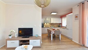 Un salon moderne avec un téléviseur à écran plat, une table à manger avec des chaises, et une cuisine en arrière-plan.
