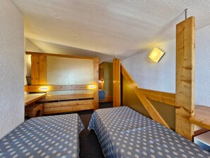 Une pièce avec deux lits, un banc en bois, un bureau et un escalier.