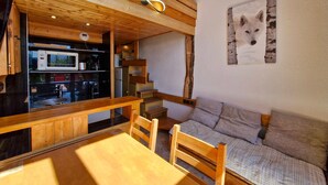 Interior de madera con una mesa de comedor, sillas, un sofá y una cocina visible a través de un mamparo de vidrio.