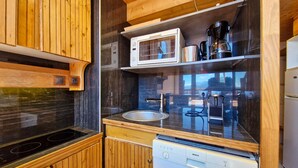 Cocina compacta con armarios de madera, lavavajillas Bosch, microondas y cafetera.