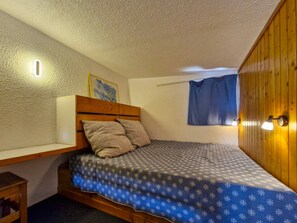 Une petite chambre avec un lit simple, une tête de lit en bois, une table de chevet et un luminaire fixé au mur.