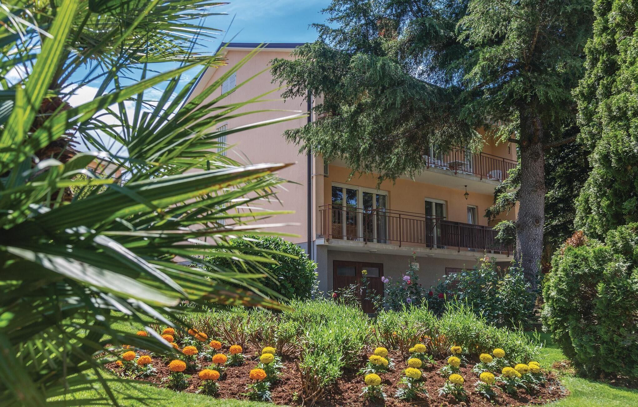 A multi-story building with balconies, surrounded by lush greenery and flowering plants.