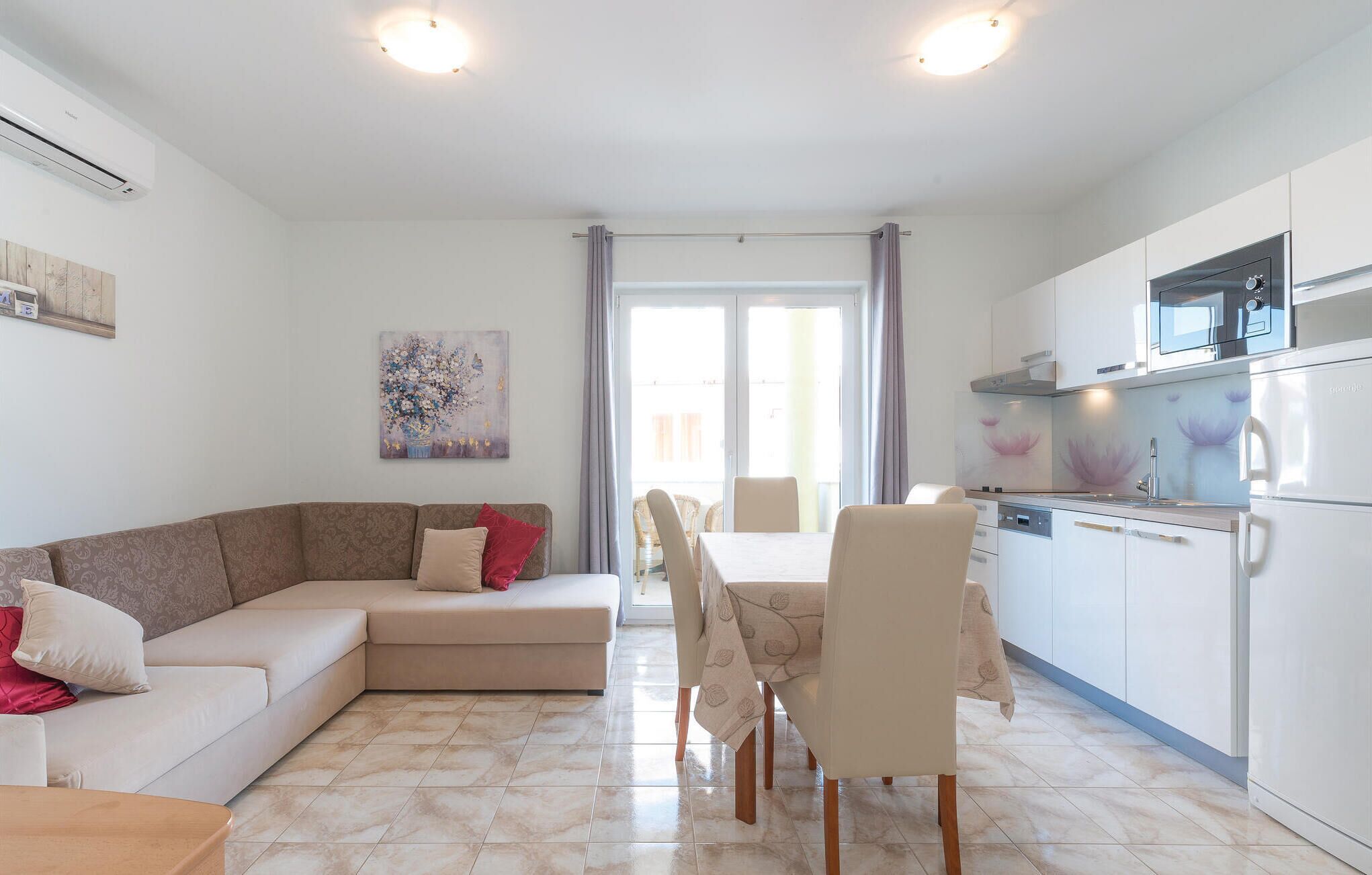 A modern living room with a sofa, dining table, chairs, and a kitchen area with appliances.