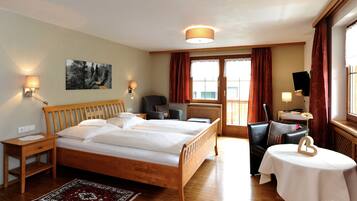 A hotel room with a wooden bed, two bedside tables, a desk, a chair, a small table with a flower vase, and a painting on the wall.