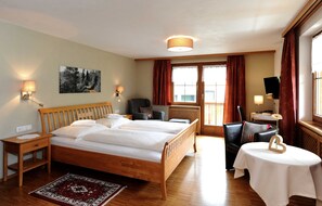Une chambre d’hôtel avec un lit en bois, deux tables de chevet, un bureau, une chaise, une petite table avec un vase de fleurs et un tableau au mur.
