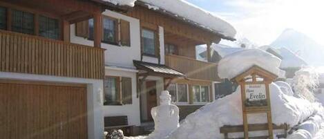 A wooden building with a snow-covered roof, a sign reading 'Hotel Evelin,' and a snowman decoration.