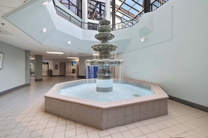 A multi-tiered fountain in a spacious indoor area with a high ceiling and a visible staircase.