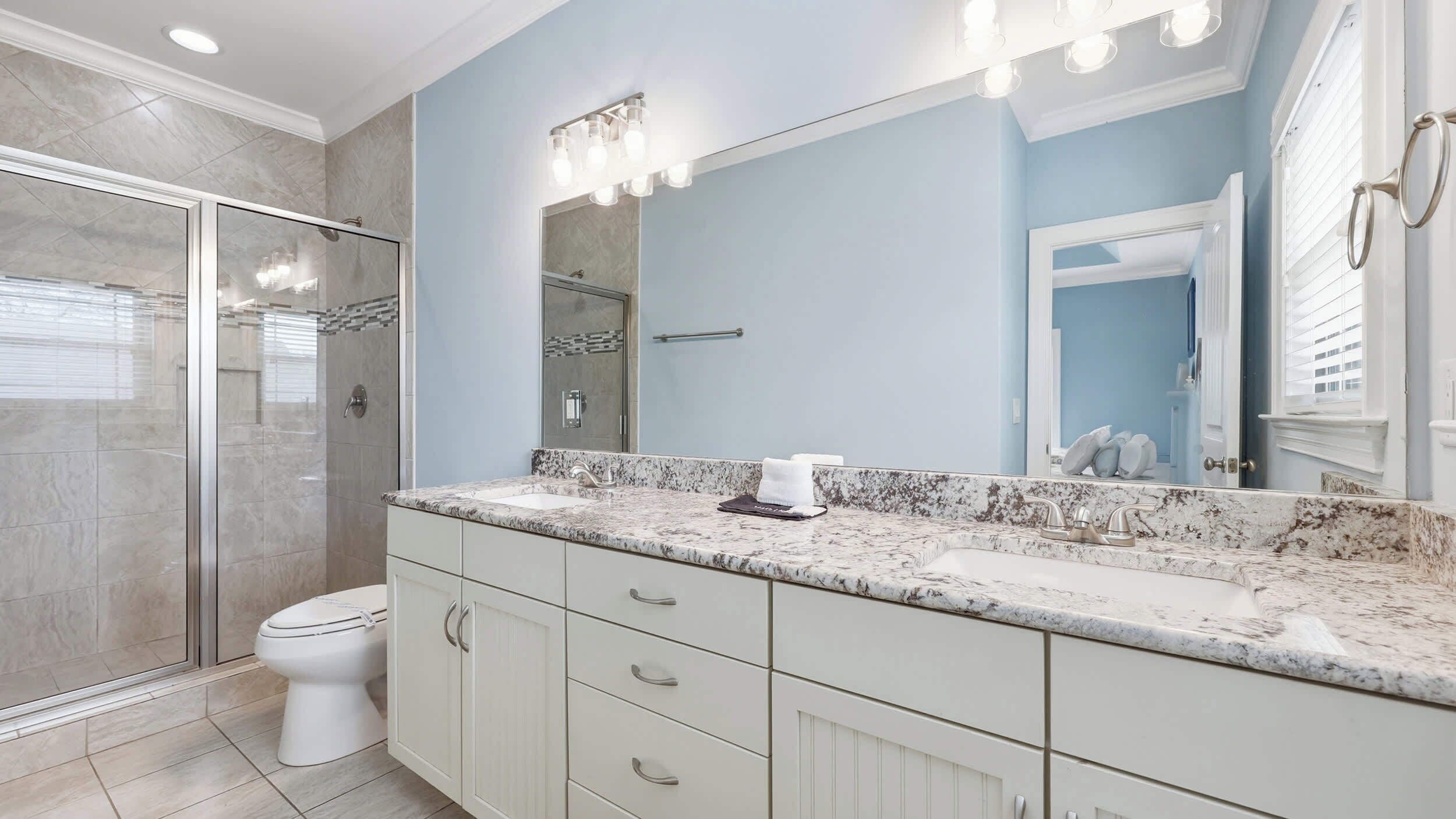 A bathroom with a shower, toilet, vanity with a sink, and a large mirror.