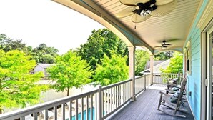 A covered porch with a pool, outdoor furniture, and a view of trees and a house.
