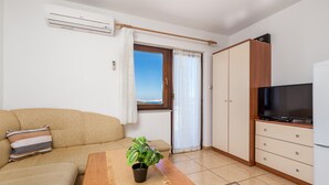A living room with a beige sofa, a wooden coffee table with a plant, a TV on a cabinet, and a window with curtains. - 1 bedroom stunning apartment in Jablanac (Jablanac)