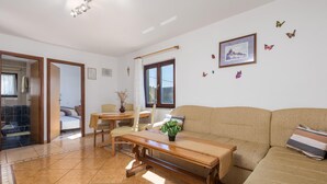 A living room with a sofa, a wooden coffee table, a dining table with chairs, and a window with curtains. - 1 bedroom stunning apartment in Jablanac (Jablanac)