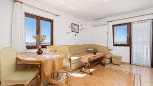 A living room with a wooden table, beige sofa, and a view of the sea through large windows. - 1 bedroom stunning apartment in Jablanac (Jablanac)