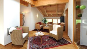 Un amplio salón con vigas de madera, muebles de mimbre y un gran ventanal.