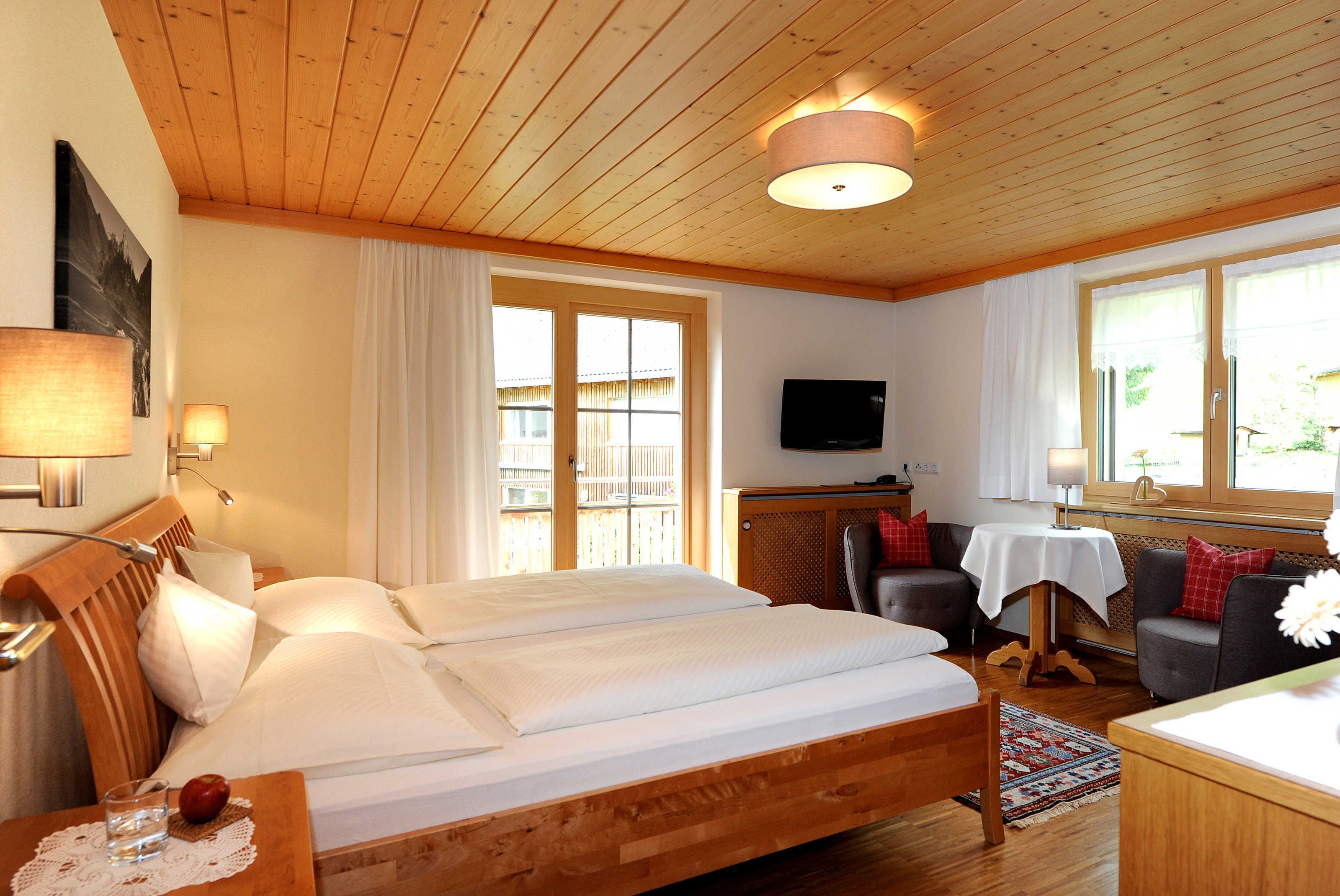 A room with a wooden bed, a television, a dining table, and a sofa.
