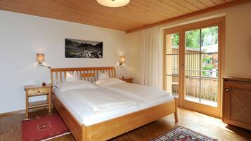 A bedroom with a wooden bed, two bedside tables, a nightstand, a red rug, a large window with a view, and a wall-mounted picture.